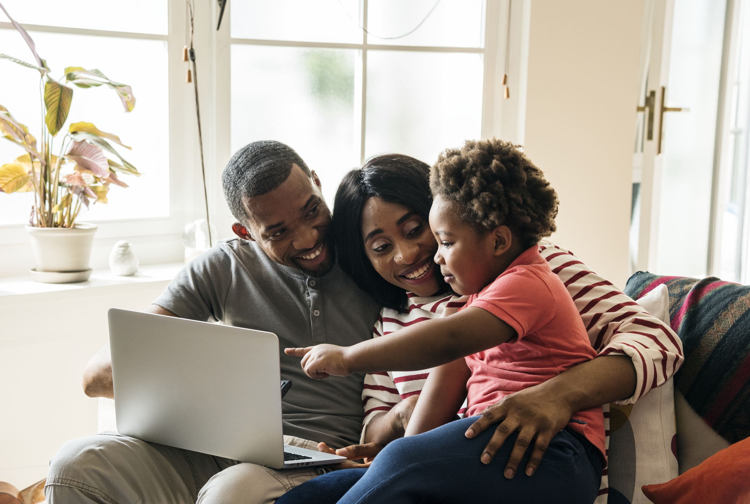 Two parents and their young child smiling together over a laptop at home