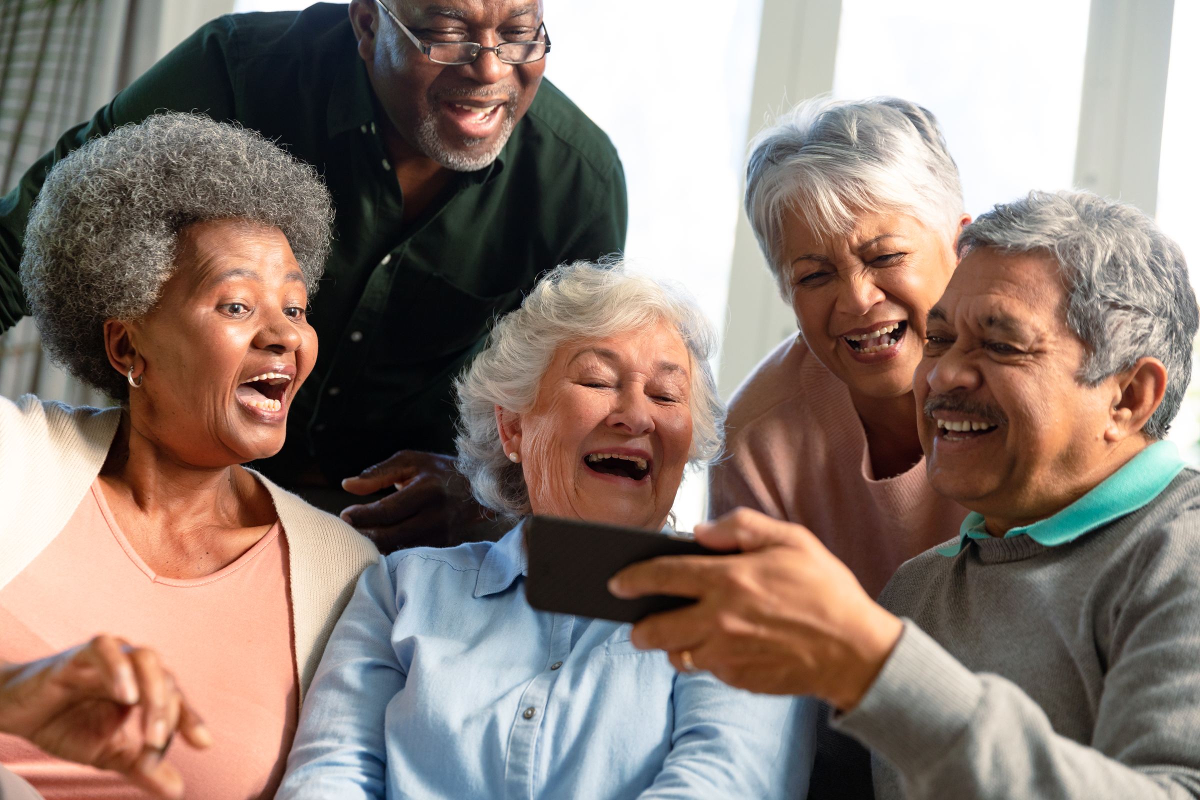 Five older friends laughing together over a phone